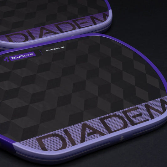 Pickleball paddle close-up: dark check pattern face with purple lettering and edge trim.