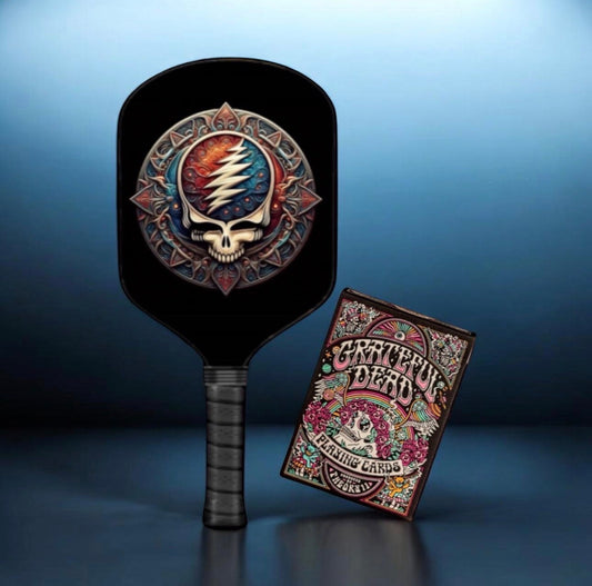 Black pickleball paddle with circular skull emblem, plus deck of playing cards