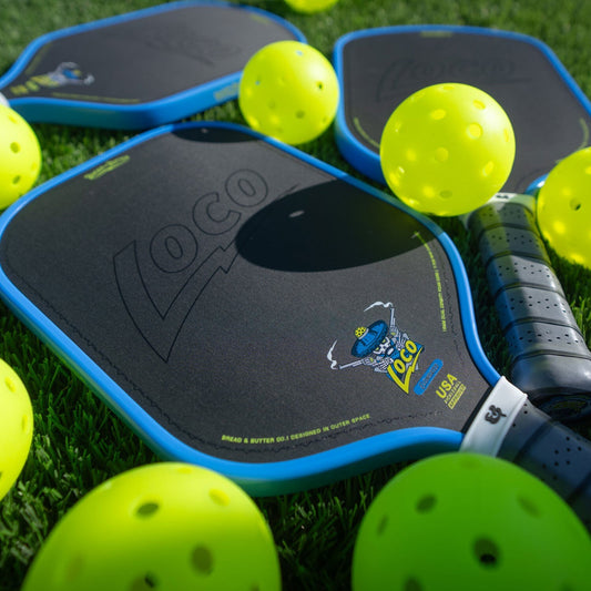 Blue-edged pickleball paddle with black face, stamped “loco” mark, surrounded by lime balls