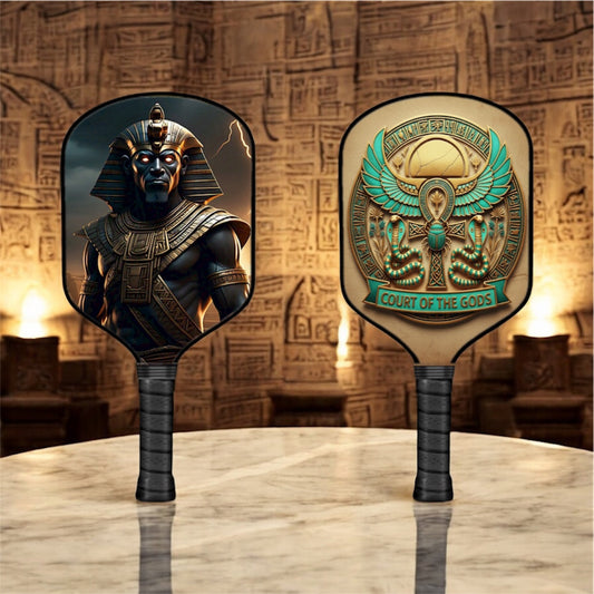 Pickleball paddle with dark face and Min god emblem in gold and teal, black grip.